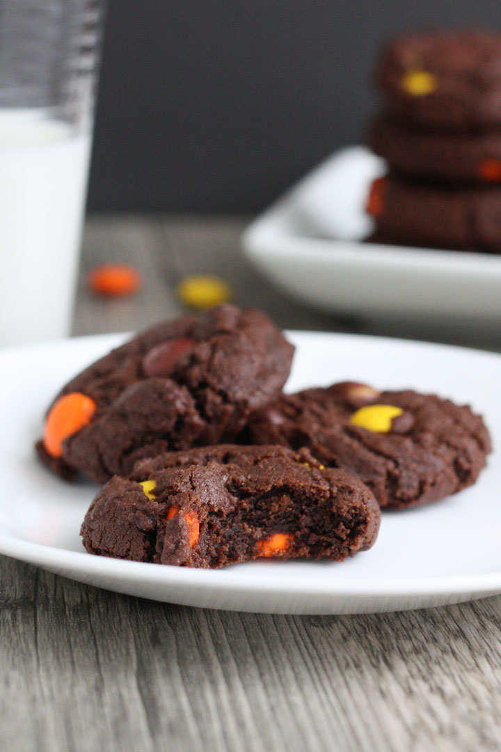 Three Reese's Pieces double chocolate cookies in white plate with bite taken out of one cookie.