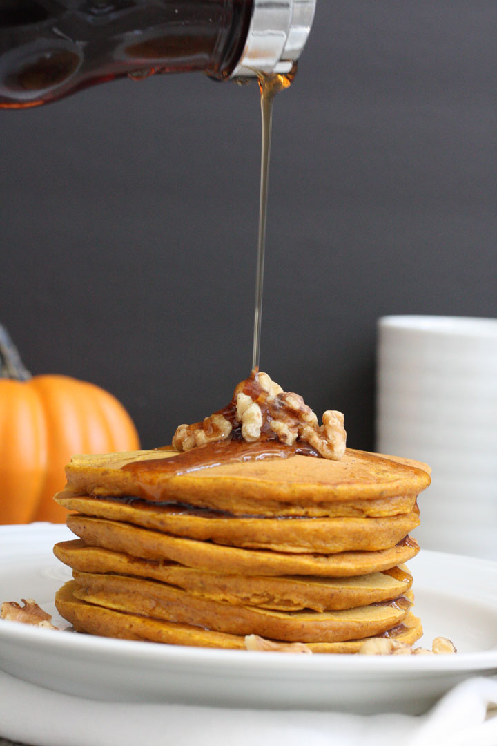 Whole grain pumpkn panckaes stack with syrup being poured over it.