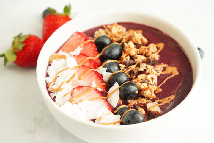 Acai bowl topped with coconut flakes, strawberries, blueberries, granola, chocolate chips and peanut butter drizzle.