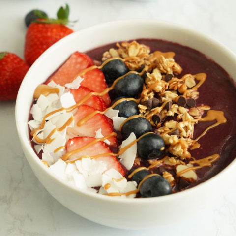 açaí bowl topped with coconut flakes, strawberries, blueberries, granola and peanut butter drizzle