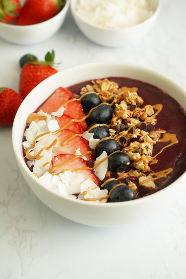 açaí bowl topped with coconut flakes, strawberries, blueberries, granola and peanut butter drizzle