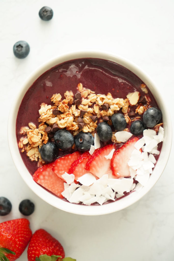 Top view of açaí bowl topped with coconut flakes, strawberries, blueberries, and granola