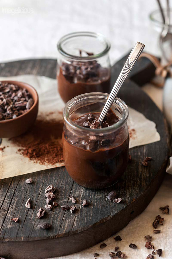 Acocado chia pudding served in glass jars with spoon on a dark wood board.