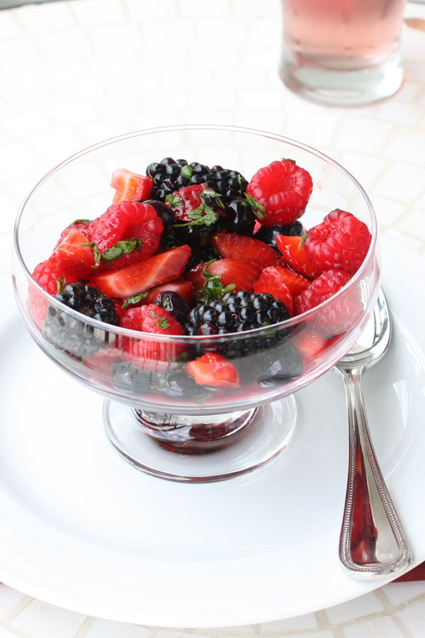 Summer berry cocktail salad in a glass bowl with spoon on the side.