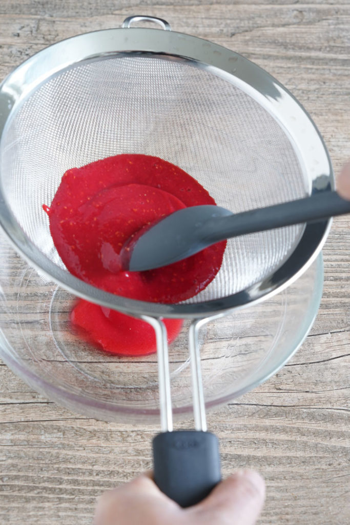 Raspberry puree being pushed through a sieve.