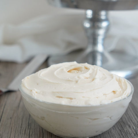 Vanilla buttercream in a clear bowl with cake in the background.