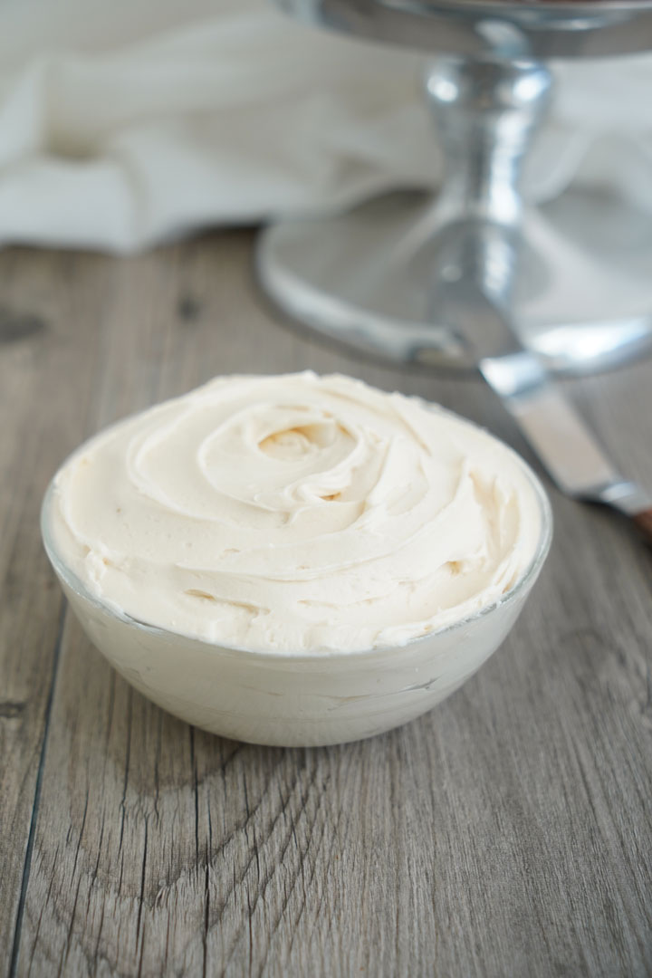 Vanilla Frosting in a clear bowl with frosting spatula in the background.