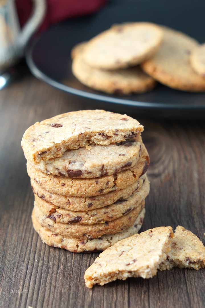 Stabel med kardemomme cookies med brukket cookie på toppen av stabelen og cookie stykker på bunnen.