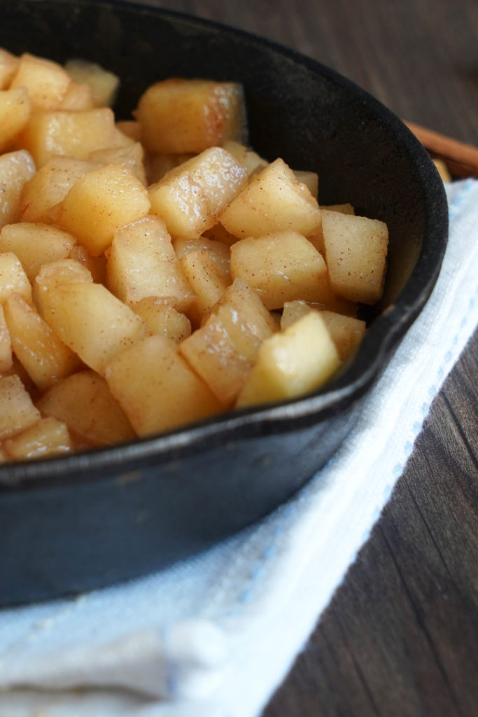 Close up of cooked apples in a skillet on top of white kitchen towel.