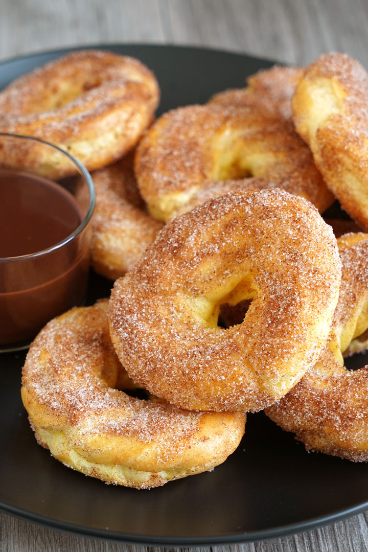 Churro donuts on a black plate with a side of chocolate sauce for dipping.