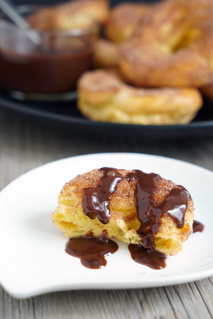 Half of churro dipped in chocolate sauce on a white plate with more churros and sauce in the background.