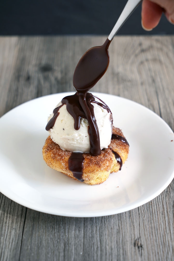 Churro Sundae being made with vanilla ice cream and chocolate sauce being spooned over top.