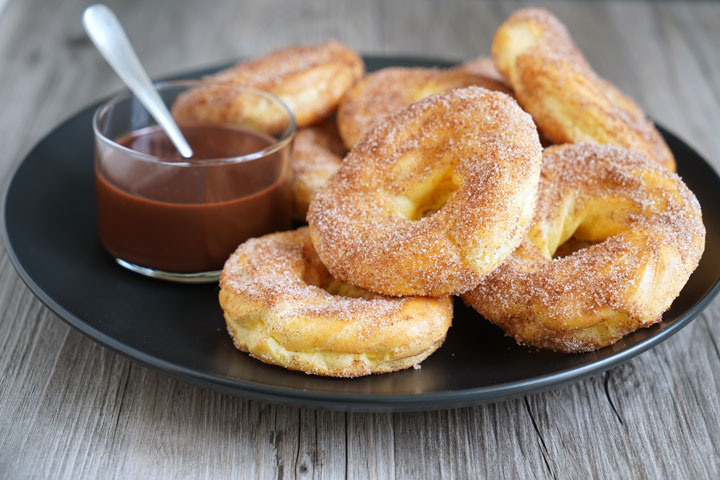 Churro donuts in a black plate with a side of chocolate dipping sauce.