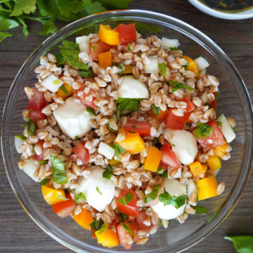 Italian herb farro in clear glass bowl, top view with cilantro and dressing on the side.