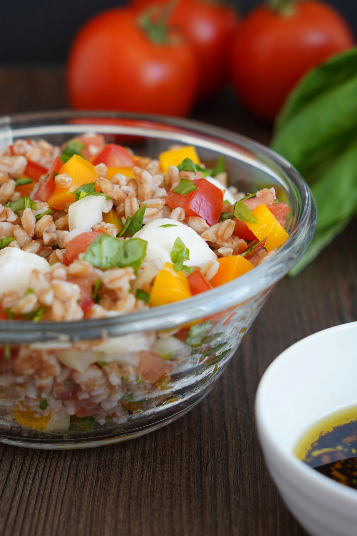 Italian herb farro in clear glass bowl with tomatoes in background.