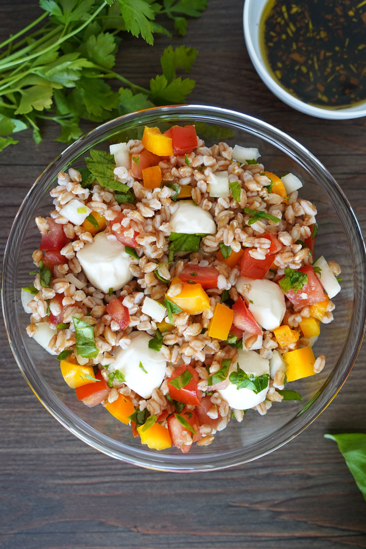 Italian herb farro in clear glass bowl, top view with cilantro and dressing on the side.