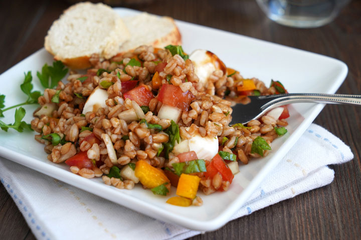 Italian herb farro salad on a white plate with bread and fork.