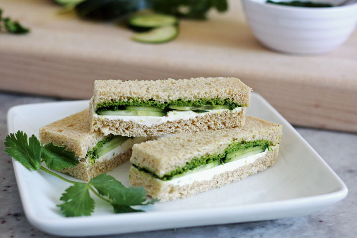 Three cucumber and mint cilantro chutney sandwiches with cilantro garnish on a white square plate.