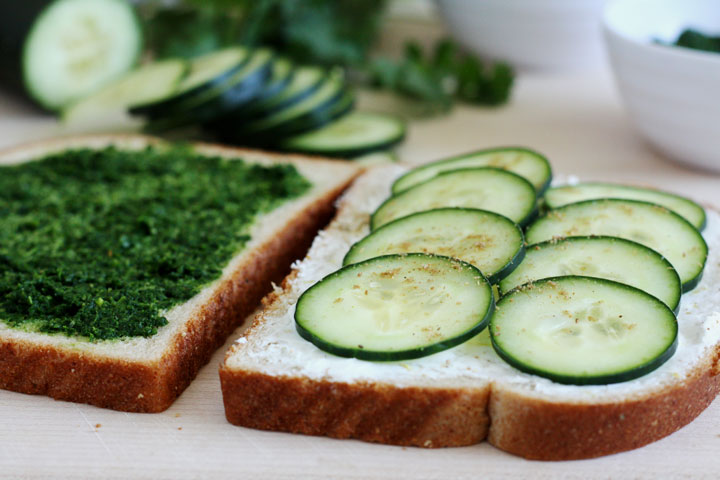 Bread slices with one showing cream cheese and cucumbers on top and the other spread with mint cilantro chutney.