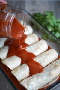 Enchilada sauce being poured onto rolled enchiladas.