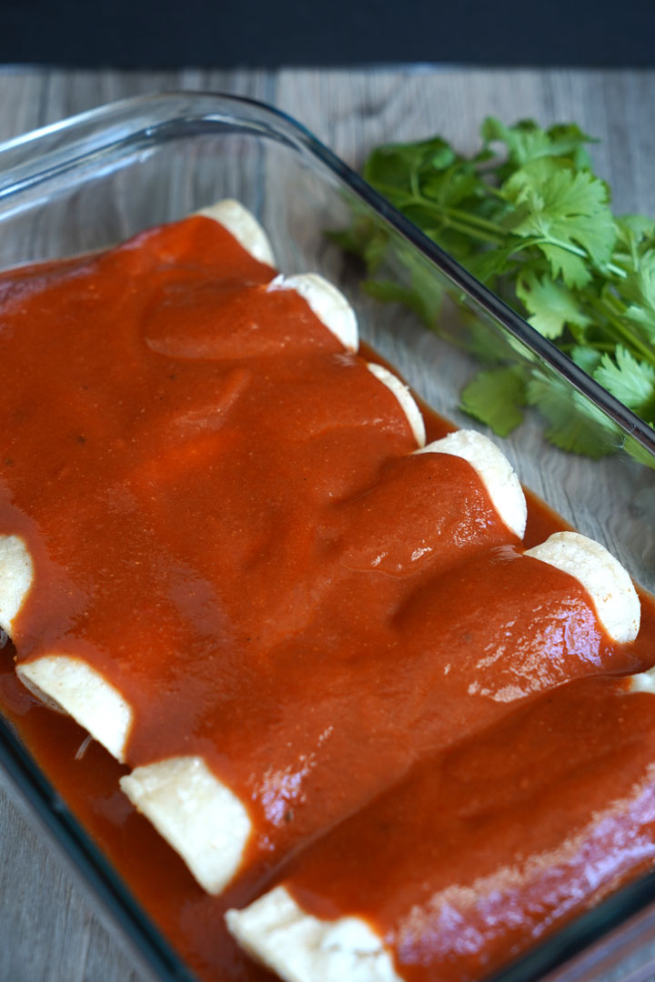 Enchilada sauce covering a tray of rolled enchiladas.