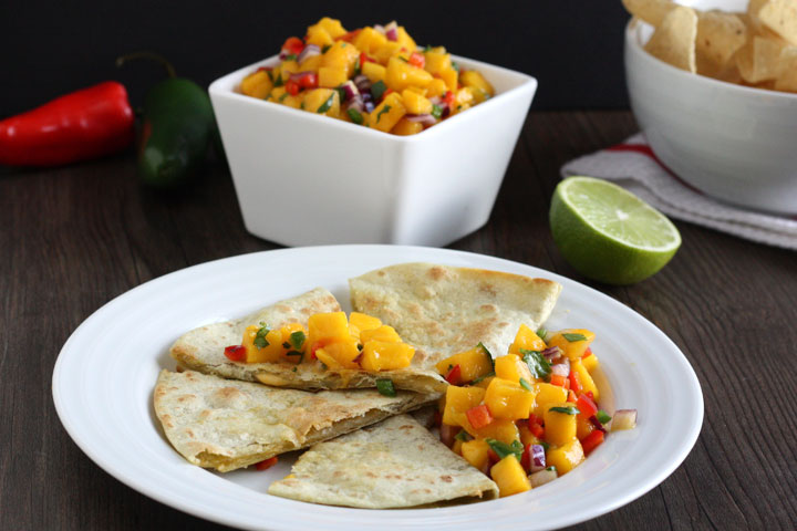 Cheese quesadillas served with mango salsa on white plate with mango salsa in square bowl in background.