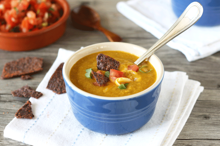 Corn soup in blue bowl on white napkin with salsa in background.