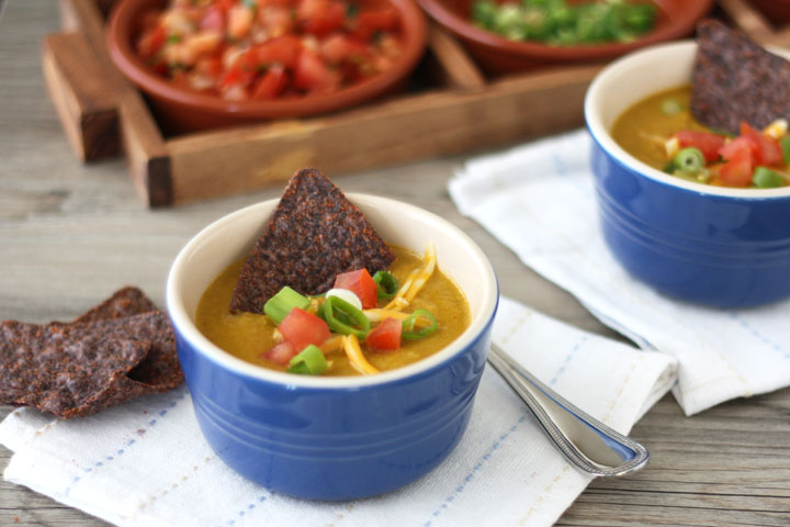 Corn soup in a blue bowl on a white napkin with blue tortilla chip garnishes. 