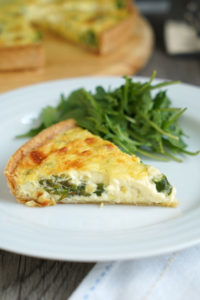 Slice of vegetable quiche with a side of greens on a white plate over a white napkin.