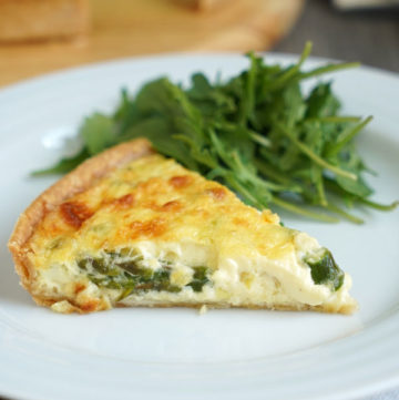 Slice of vegetable quiche with a side of greens on a white plate over a white napkin.