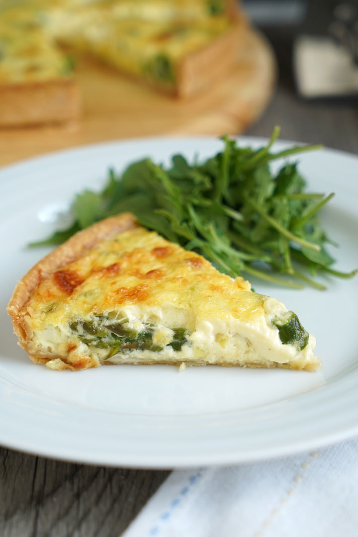 Slice of vegetable quiche and greens on a white plate over a white napkin.