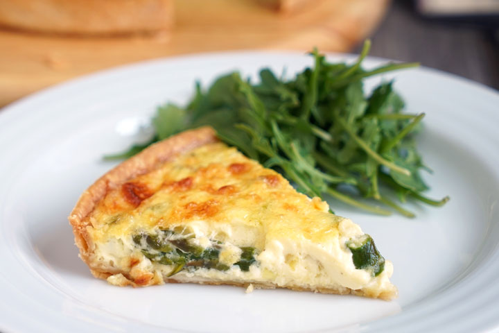 Slice of vegetable quiche with a side of greens on white plate.