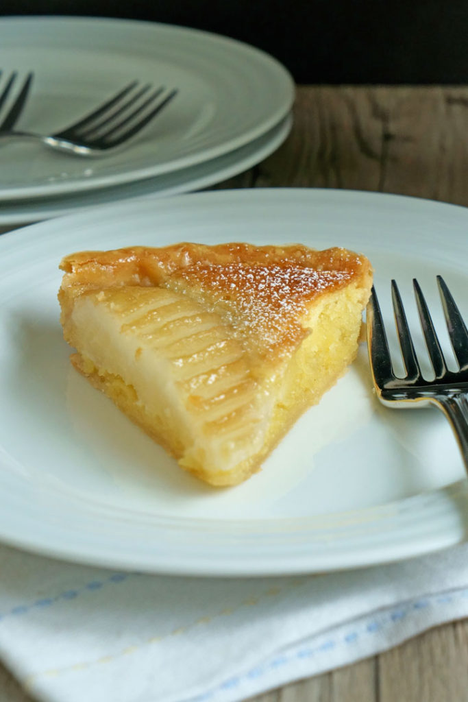 Slice of pear and frangipane tart in a white plate with a fork. 