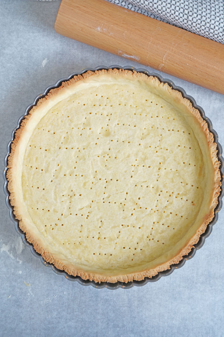 Top view of empty baked tart crust with rolling pin on the side.