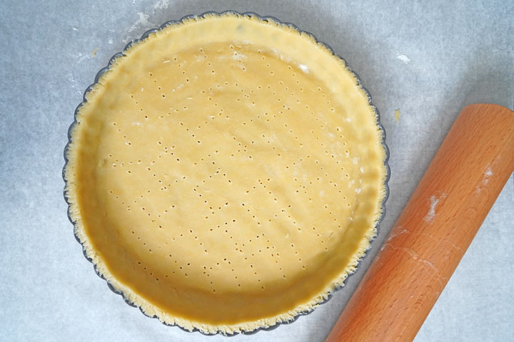 Top view of raw tart dough in in tart pan with holes pricked on the bottom.