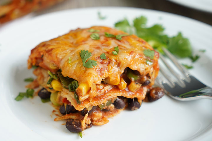 Slice of vegetarian enchilada casserole on white plate with fork and cilantro garnish.