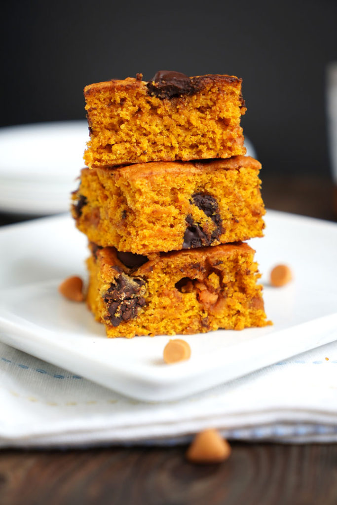 Three butterscotch pumpkin cake bars stacked on top of each other on a white plate.