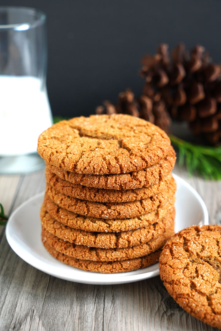 Stack of gingersnap cookies on a white plate with milk glass in the background.