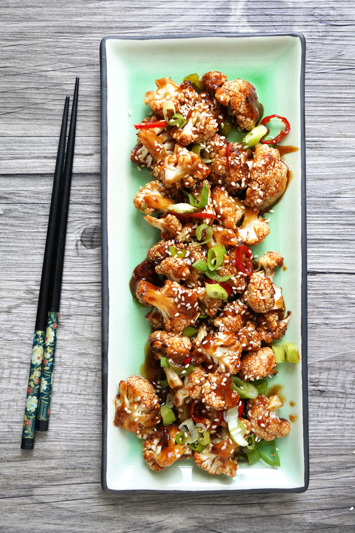 Overhead view of Kung Pao Cauliflower on green rectangular plate with chopsticks to the side.