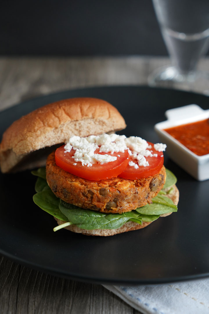 Open lentil burger on whole wheat bun topped with tomato and feta. 