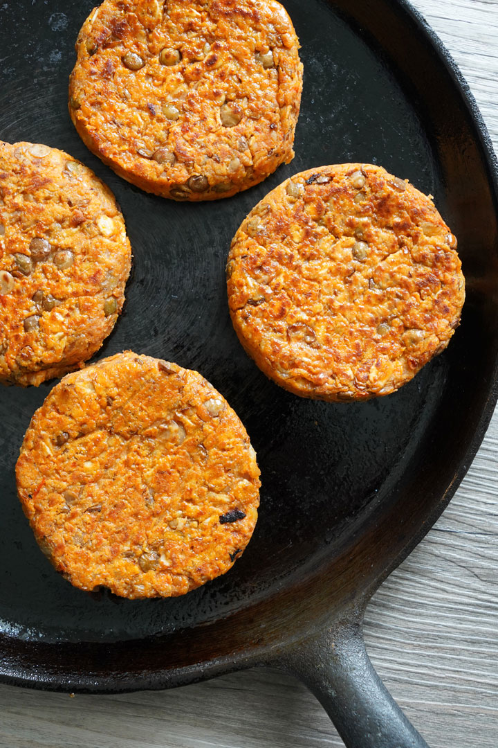 Lentil burgers cooking on a cast iron skillet.