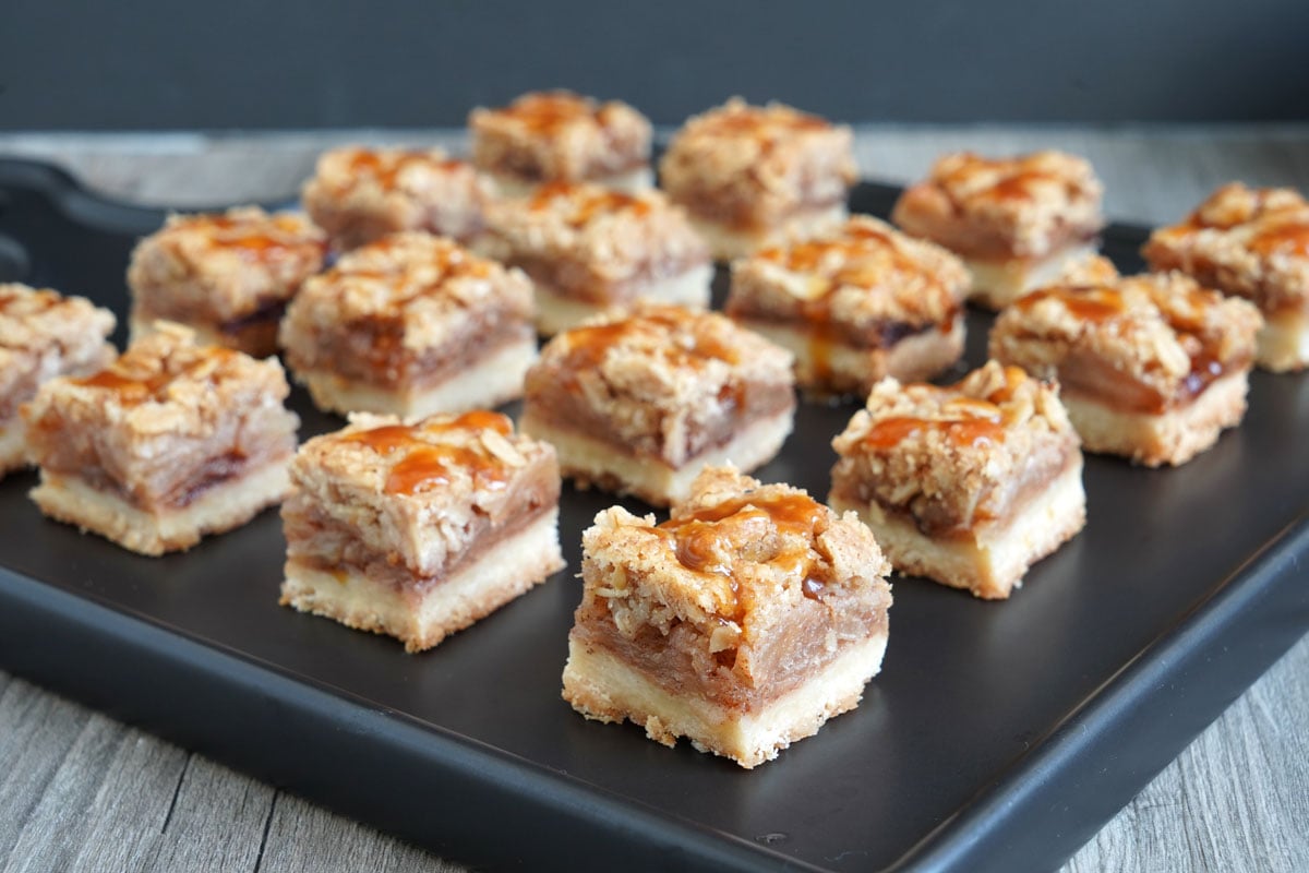 Baked salted caramel apple pie bars cut into small squares on a black tray.