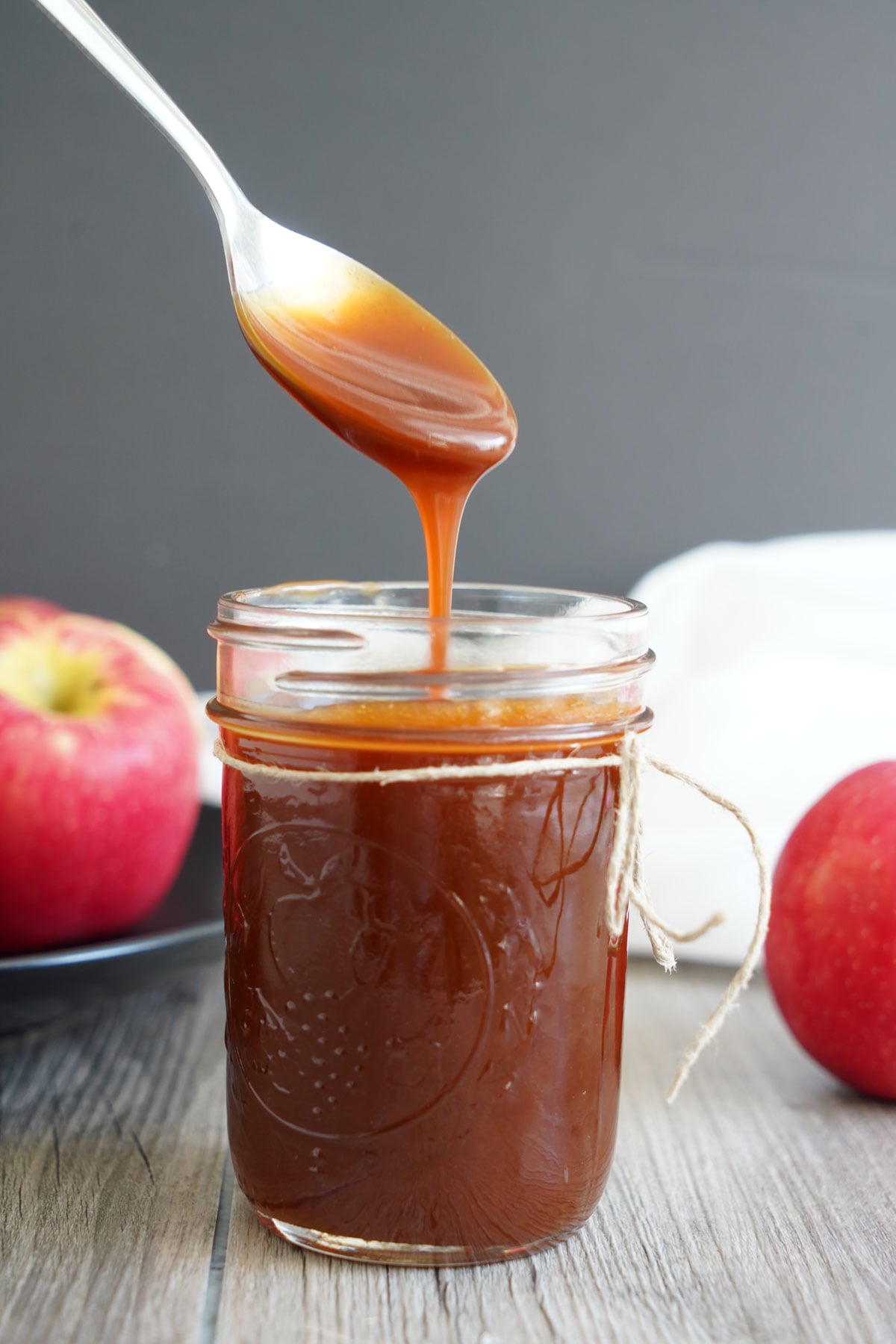 Caramel sauce dripping off a spoon into a glass jar of more sauce.