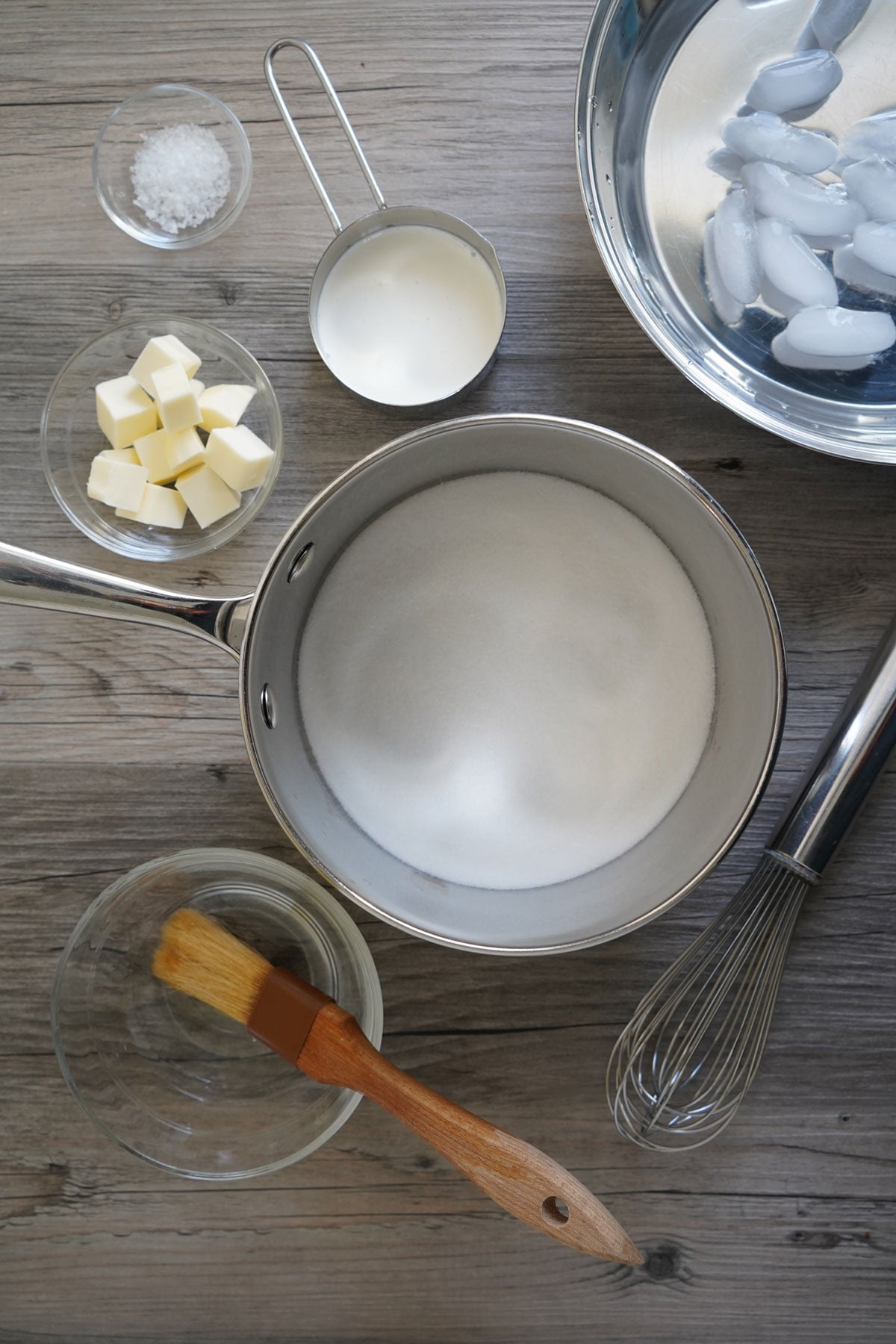 Ingredients and equipment needed for salted caramel sauce: pot, sugar, cubed butter, sea salt, heavy cream, pastry brush, water, whisk, ice bath.