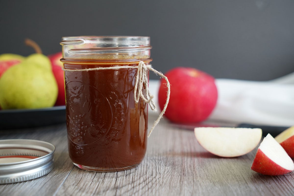 Salted caramel sauce in a jar with apples in background.