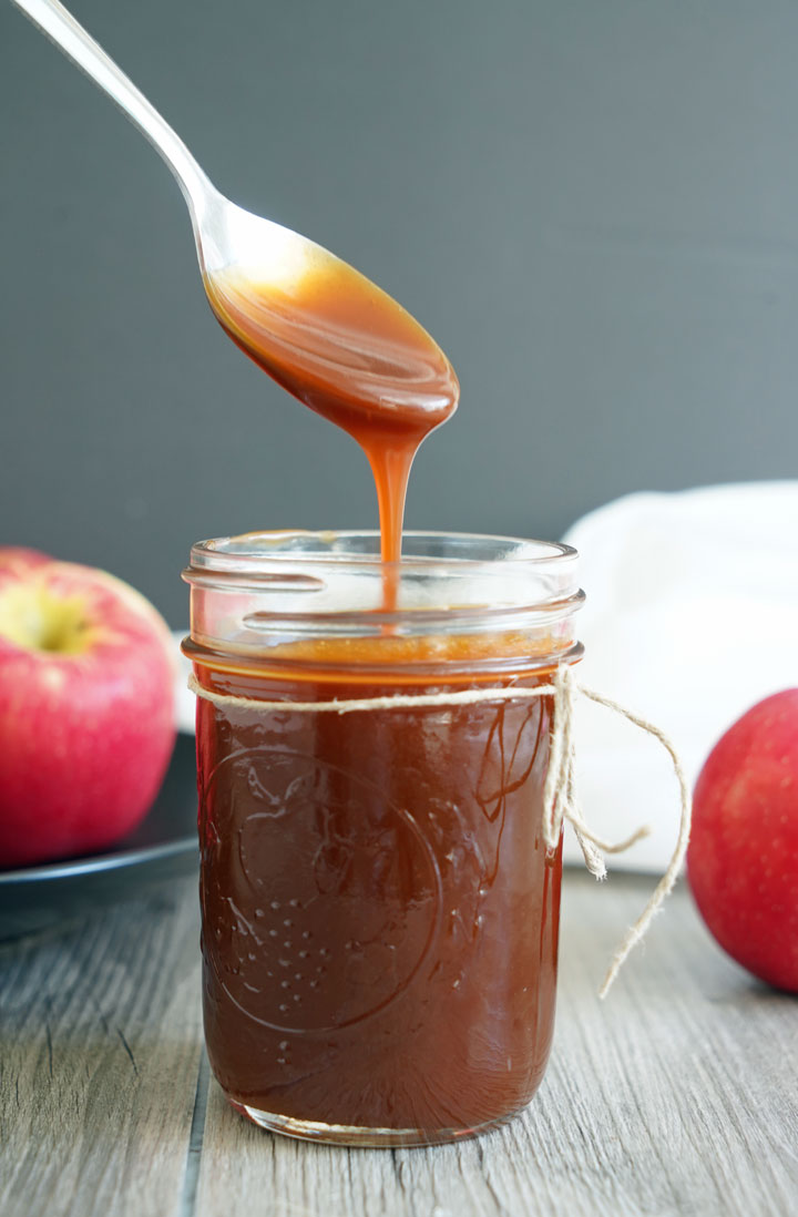 Caramel sauce dripping off a spoon into a glass jar of more sauce.