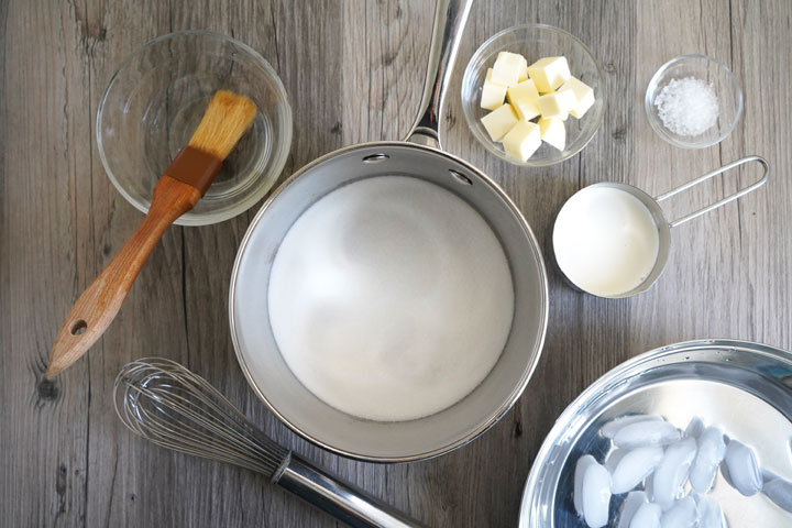 Ingredients and equipment needed for salted caramel sauce: pot, sugar, cubed butter, sea salt, heavy cream, pastry brush, water, whisk, ice bath.