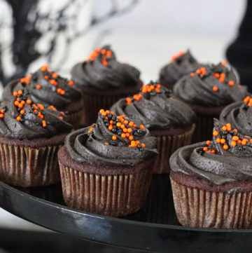 Chocolate cupcakes frosted with black frosting and orange and black sprinkles with halloween themed background..