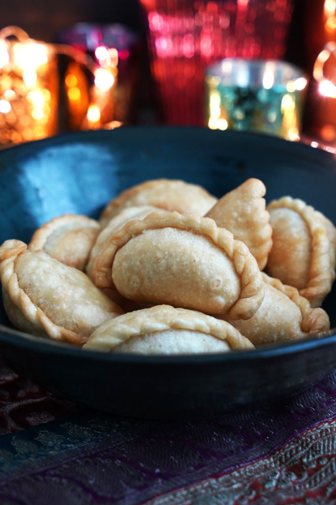 Fried ghugra in a blue bowl with diwali lights in background.