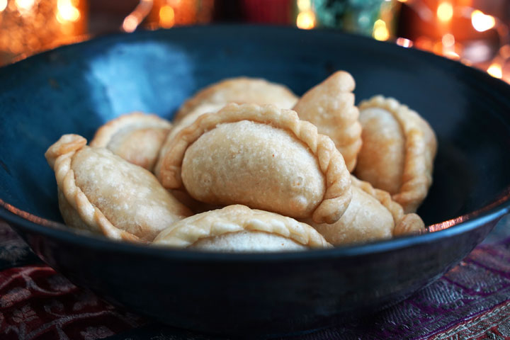 Fried ghugra in a blue bowl with diwali lights in background.